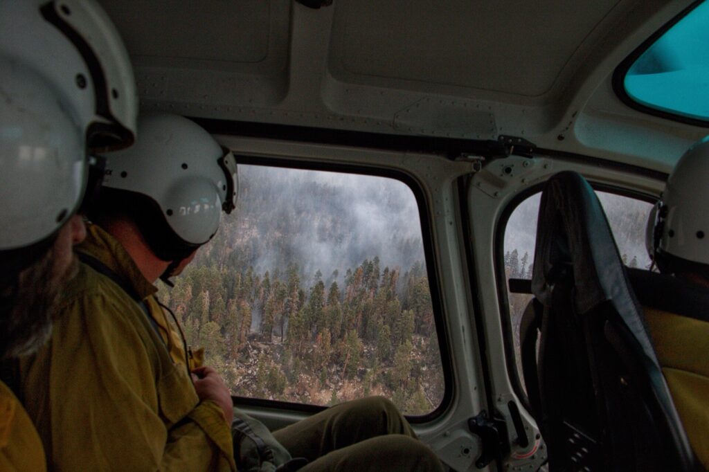 Firefighters look out from a helicopter at wildfire smoke rising from forest in Yosemite National Park